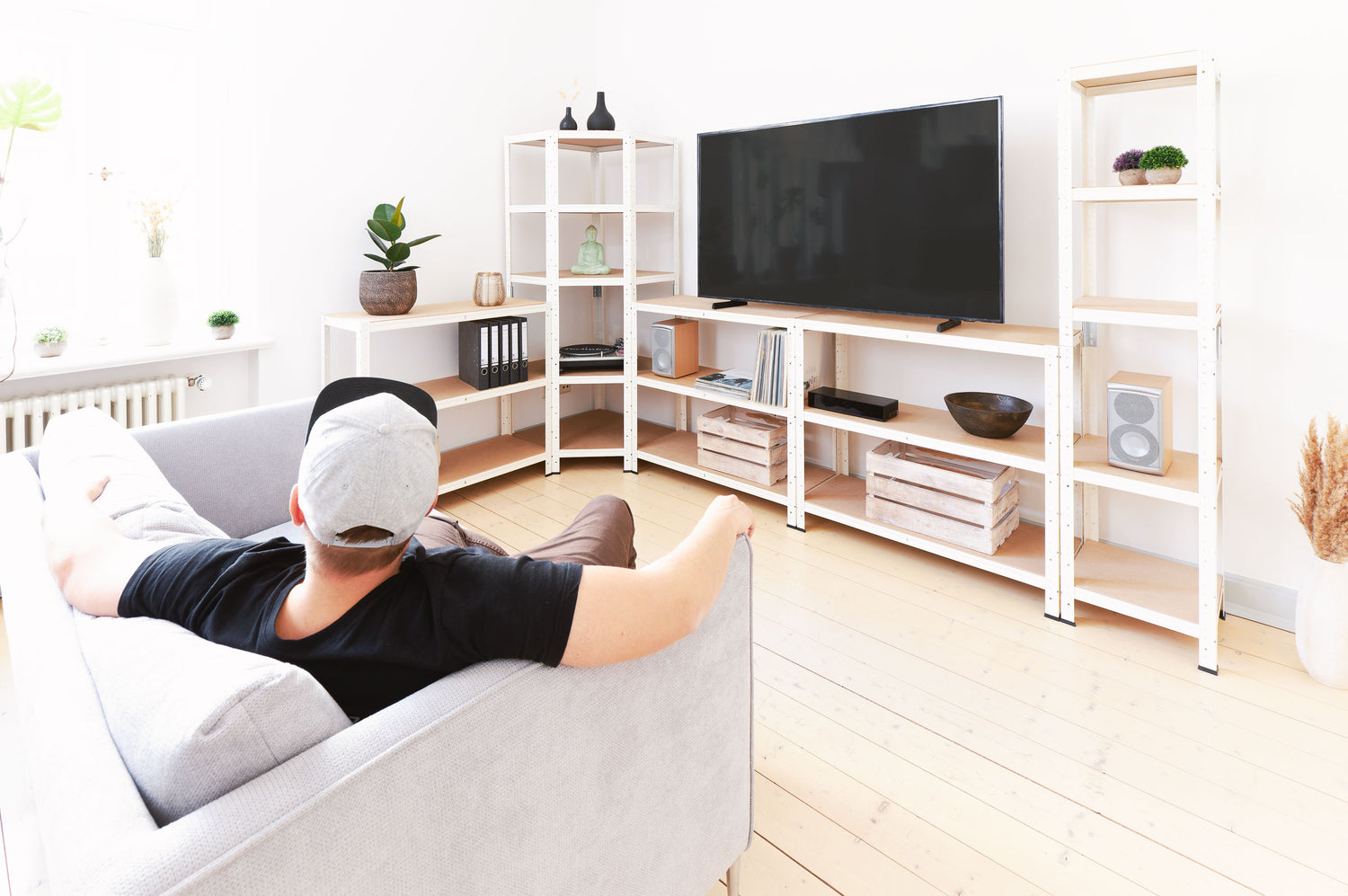 Person auf Couch vor Wohnzimmerregalwand mit Fernsehen und Dekoration